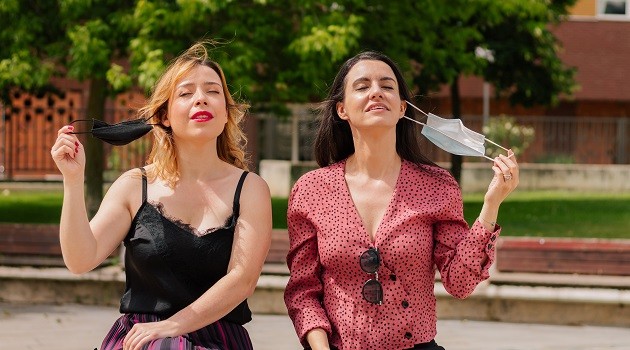 Two women taking off their masks on the street. Concept end of the mandatory outdoor mask. End of the pandemic. Friends.