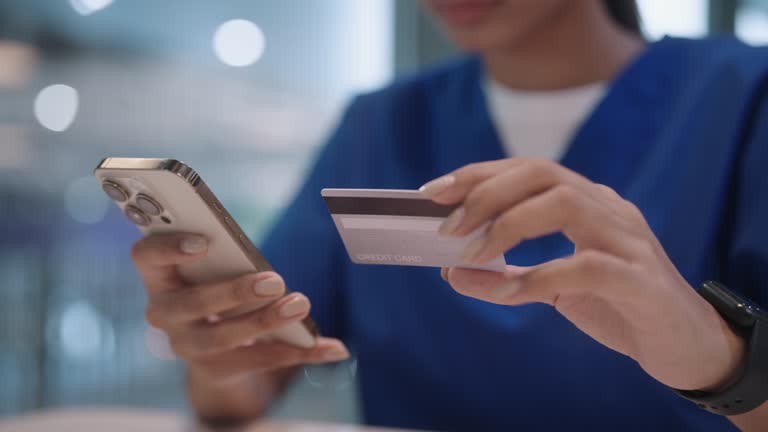 Unrecognized person in medical scrubs using a smartphone and credit card for online payment.