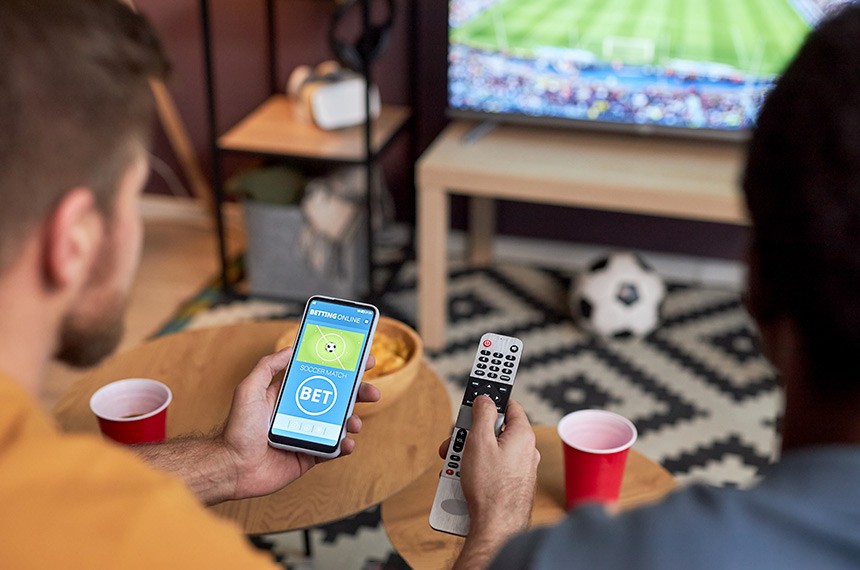 Close up of two men watching football match on TV and holding smartphone with online sports bets ------ Close up de dois homens assistindo jogo de futebol na TV Foto iStockphoto
