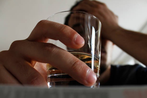 Drunk young adult male holding glass of alcohol, studio shot.